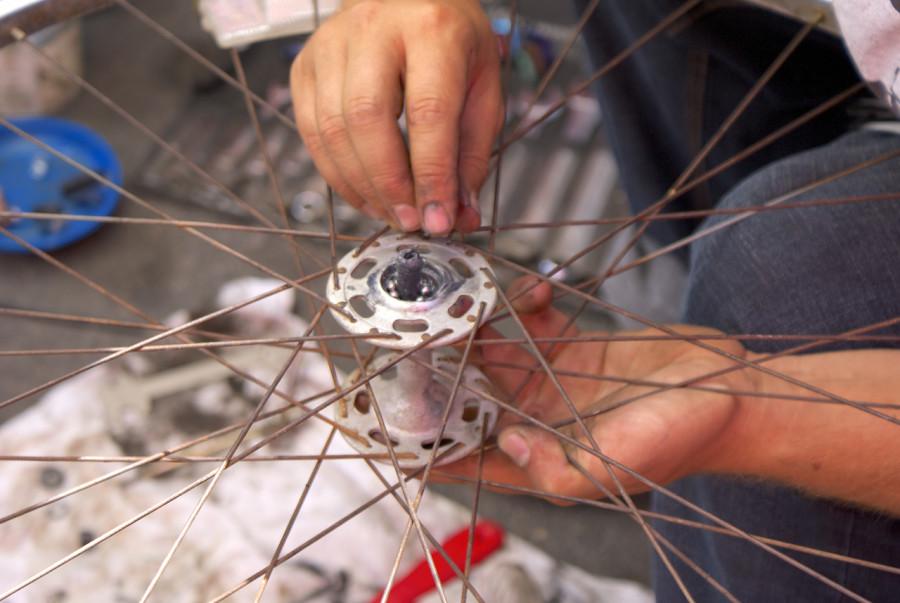 A visitor at the Bikes del Pueblo tent of the City Heights Farmers Market changes the bearings in the axle of a wheel from his bike with help and guidance from volunteers on April 18. Photo credit: Torrey Spoerer