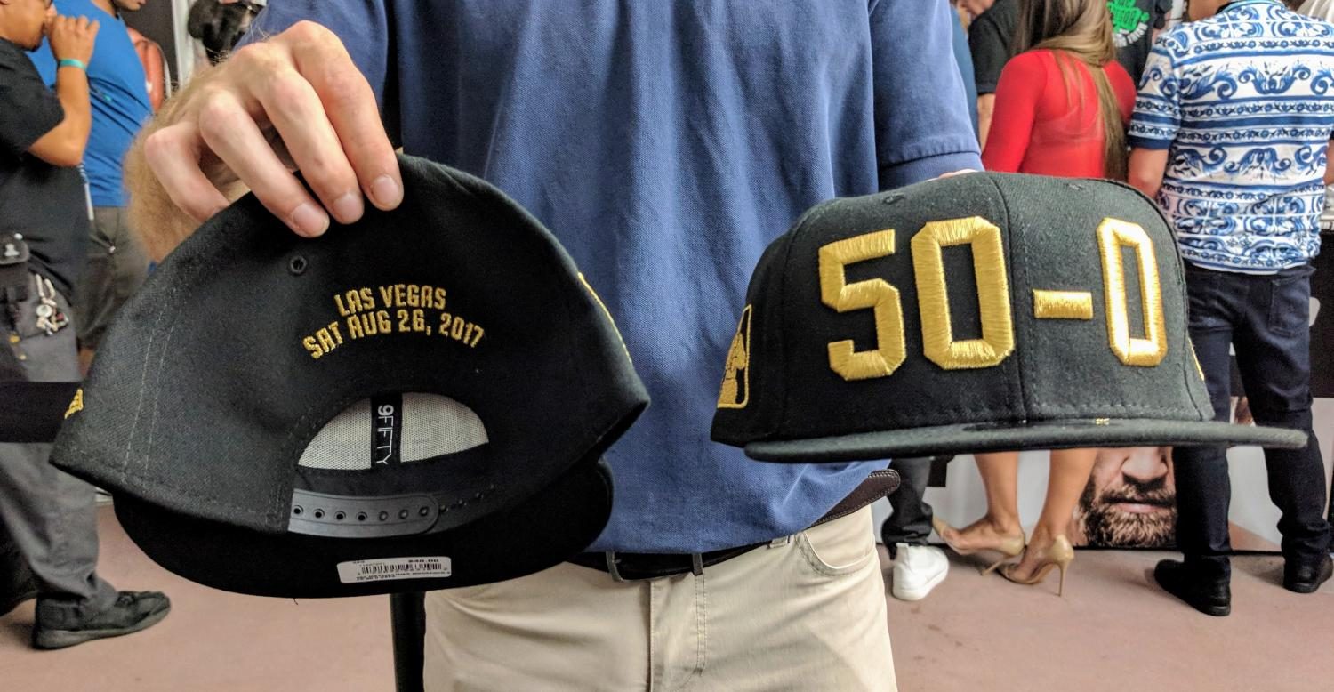 A man holds up the front and back of a baseball cap that mark Floyd Mayweathers record of 50-0