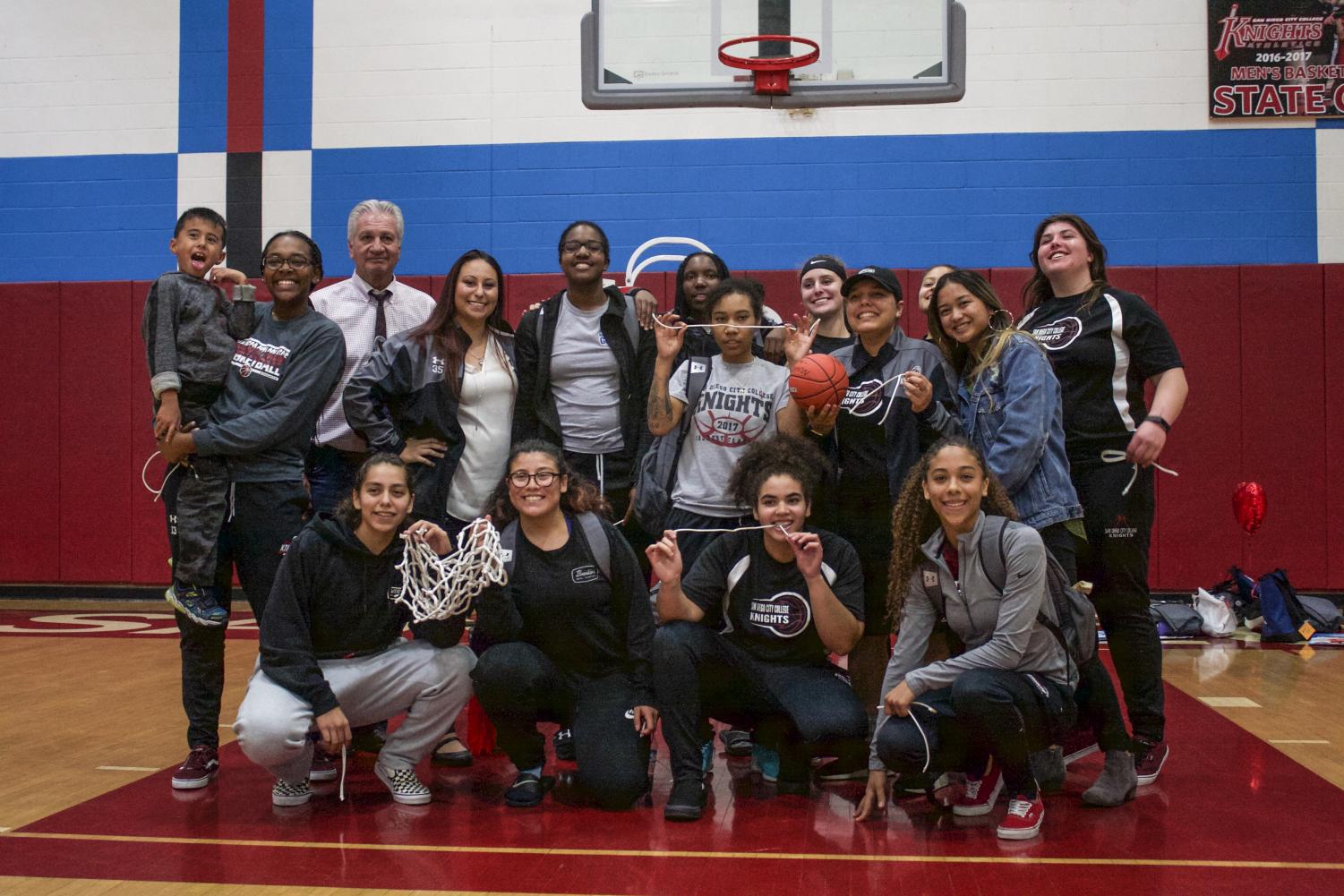 City College's Women's Basketball team, pose for a team picture behind the basketball net they cut in honor of their sophomore night and season. 