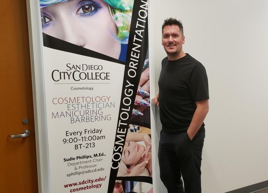Michael eceltka stands in front of an ad for the City College cosmo program.