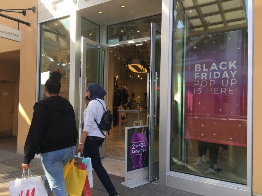 Women at a mall walk aoutside of a store advertising a black friday sale.