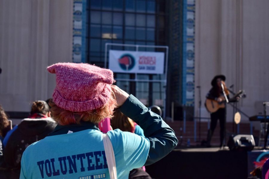 Volunteer of the Womens March with a blue shirt than the representative pink hat of the Womens March, looking at the stage.