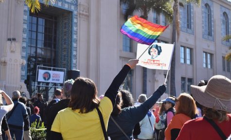 Women with a yellow shirt waving an LGBTQ+ rainbow flag in the crowd.