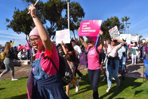 Women n pink shirts holding signs.