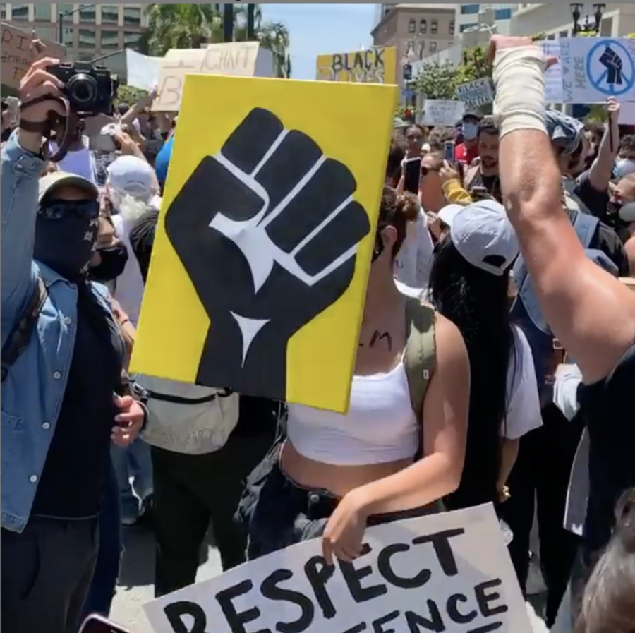 Protest against police brutality in San Diego, CA. Picture shows crowd and a yellow sign with a black fist.