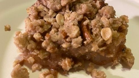 A dessert crumble made with pears and oatmeal sits on a cream colored eating plate