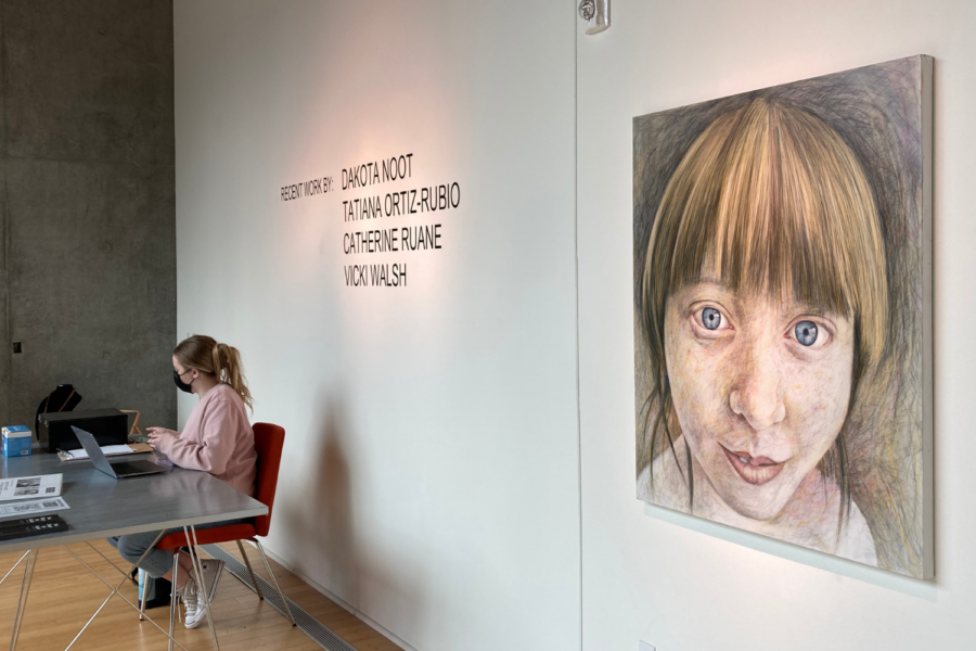 A woman sits next to the portrait of a face at the entrance of an art gallery.