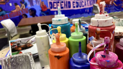 Bottles of bright paint sit on a table in the City College cafeteria in front of a mural