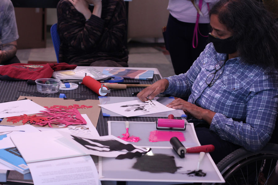 Artist Bhavna Mehta demonstrates cut paper art and printmaking to a group of people.