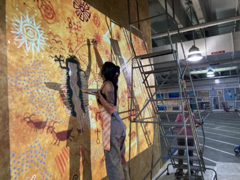 Sasha Sanudo reaches a paintbrush to the top of the AH Building garage mural while Terri Hughes-Oelrich looks at the mural from behind a step ladder