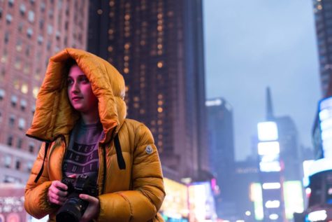 Rachel Karalnik stands in front of skyscraper buildings in New York City while holding a camera.