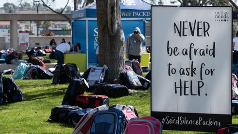 Sign promoting mental health awareness surrounded by backpacks and students