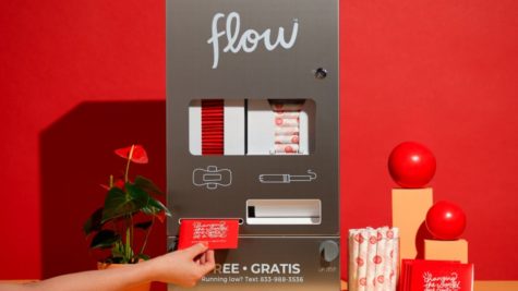 A person retrieves a menstrual pad from a silver Aunt Flow dispenser