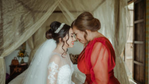 Katya Echazarreta wearing a white wedding dress and veil (left) stands and touches foreheads with her mother Liliana Martin wearing a red dress (right) on her wedding day in 2022.