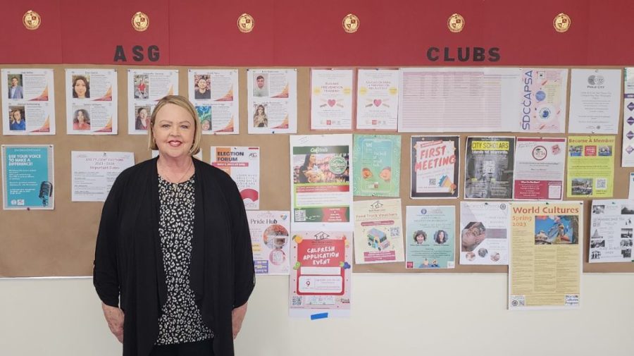 Student Affairs Coordinator and ASG Advisor Lori Oldham stands in the M building in front of a wall of posters