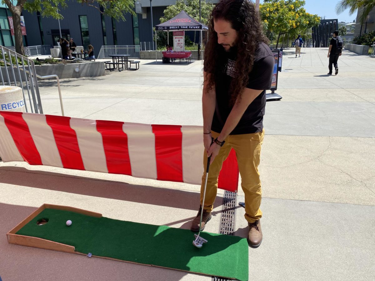 City Times Editor-in-Chief Marco Guajardo putts a ball at the Club Rush Carnival. Other attractions included a crossbow shooting game and snow cones, August 24, 2023. Luke Bradbury/City Times Media