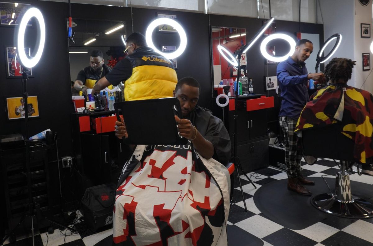 Barber Larry Jackson, far left, rearranges his equipment while Darius Manney, 22, center left, sees his new haircut during the Fresh Cutz barbershop grand opening in San Diego City College, April 23, 2024. I think (the barbershop) is good because students are already on campus, so if they want to get a haircut, they can easily come down here, Manney said. Photo by Keila Menjivar Zamora/City Times Media