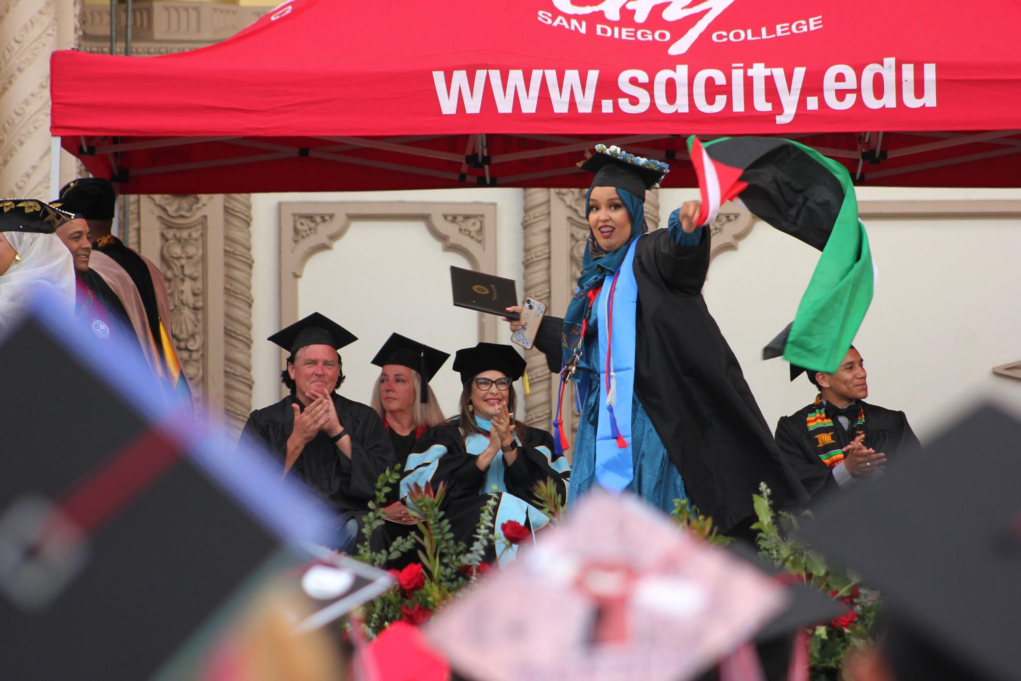 A graduating student waves a Palestinian flag as she crosses the stage at the San Diego City College commencement, Thursday, May 23, 2024. Photo by Bailey Kohnen/City Times Media