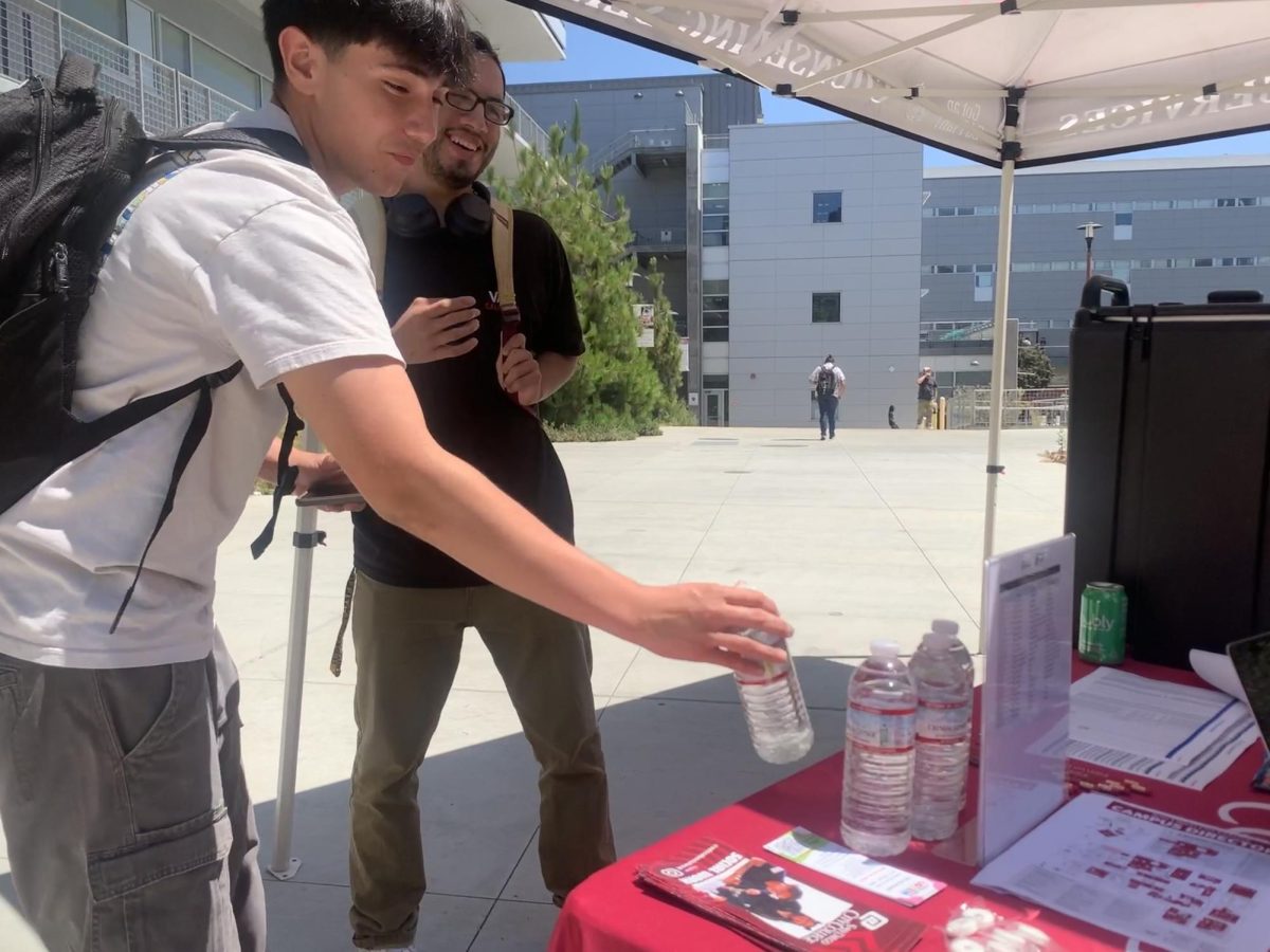 Estudiante de segundo año de ingeniería civil, Adrián Vargas, a la izquierda, toma una botella de agua en una carpa de bienvenida el miércoles 20 de agosto de 2024. En un correo electrónico a City Times, la Coordinadora de Alcance, Clarissa Padilla, dijo que las carpas de bienvenida con recursos para estudiantes, incluyendo agua, solo están disponibles de lunes a jueves durante la primera semana de clases. Foto por Keila Menjivar Zamora/City Times Media