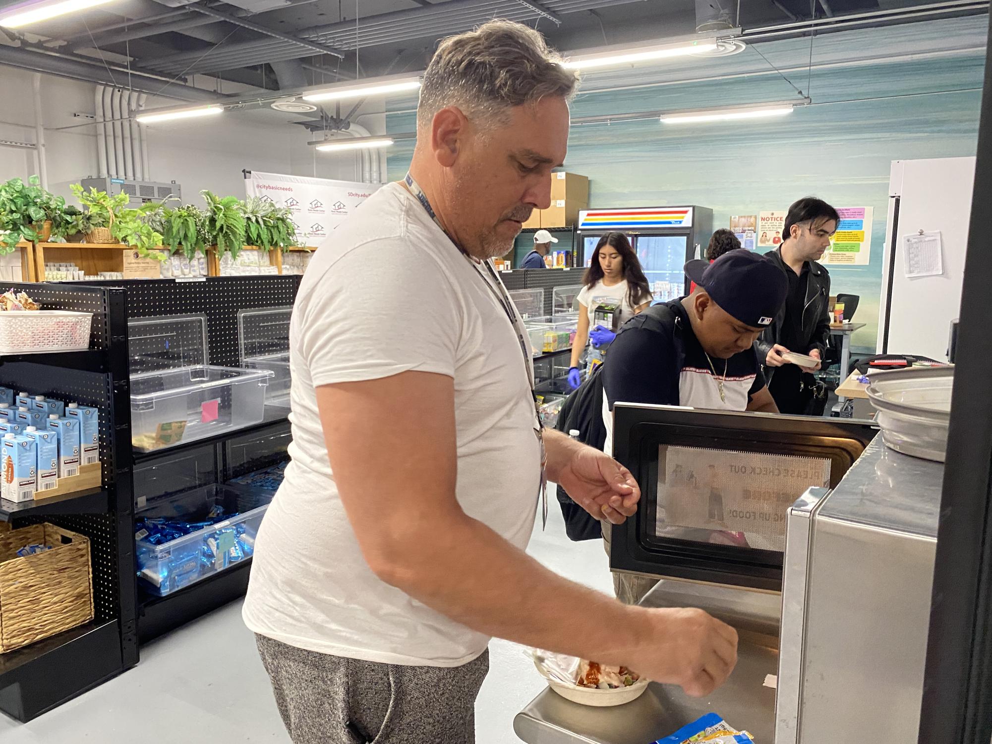 Guillermo Cabanellas, a la izquierda, de 51 años, calienta su comida en la despensa de alimentos, Knights’ Table, el 26 de agosto de 2024. Como estudiante de gestión de información de salud, visita el centro cuatro veces a la semana para obtener sus comidas. Foto de Luke Bradbury/City Times Media