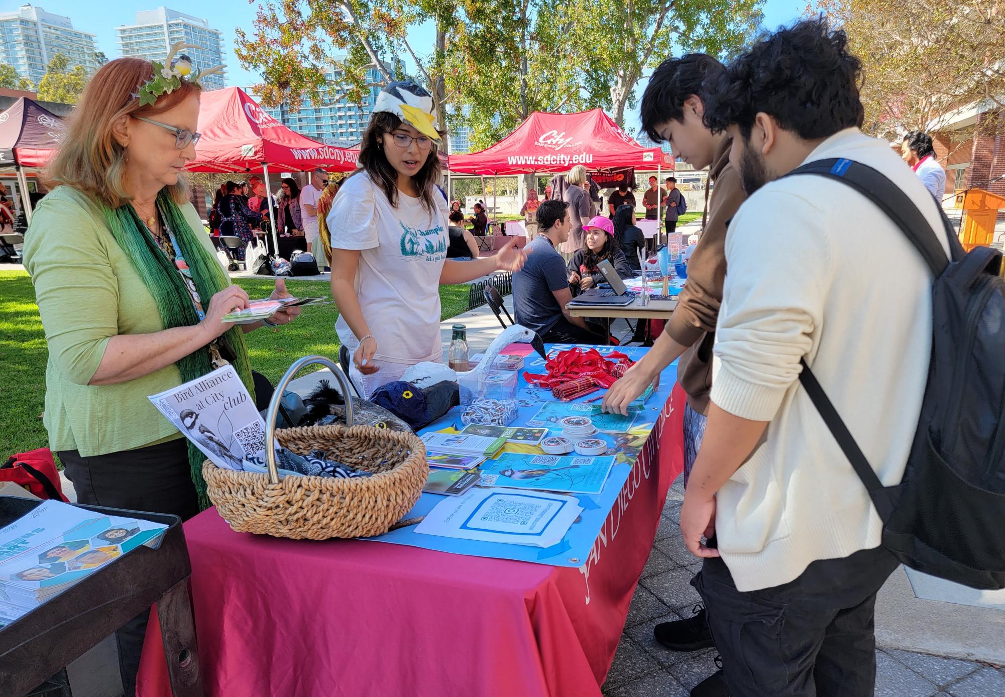 Members of the Bird Alliance group at City College Lisa Chaddock, left, and Daisy Navarrete, center, entice interested students to join by detailing what an average meeting looks like and showing off handcrafted papier-mâché bird hats during the Halloween Bash & Club Rush at City College in the Curran Plaza, Thursday, Oct. 31, 2024. Photo by Jordan Bell/City Times Media