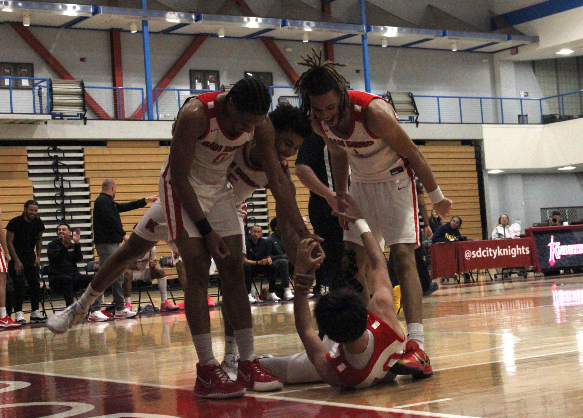 City College men’s basketball player Pharaoh Amadi, left, Santana Huff, center, and Micah Brickner, right, help up Matin Madadkar, bottom center, after a defensive foul at Harry West Gym, Wednesday, Jan. 28, 2026. The players celebrated the possibility of a 3-point play from the foul call. Photo by Nadia Lavin/City Times Media