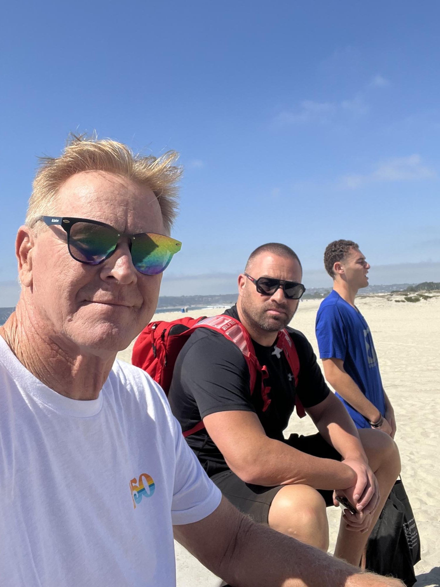 Rusty Smith, left, sits with Mitch Charlens, center, and his son Brandon Charlens, right, at Coronado Beach in an undated photo. Photo courtesy of Erin Charlens